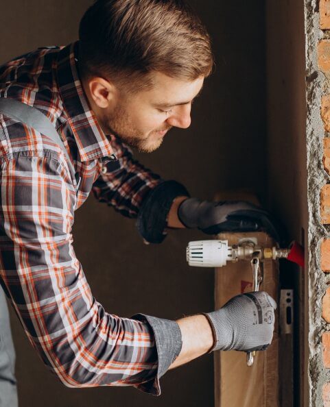 man in plaid shirt wearing gloves holding wrench working on pipe in home